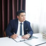 Professional businessman in a suit contemplating while sitting at a desk in a bright office.